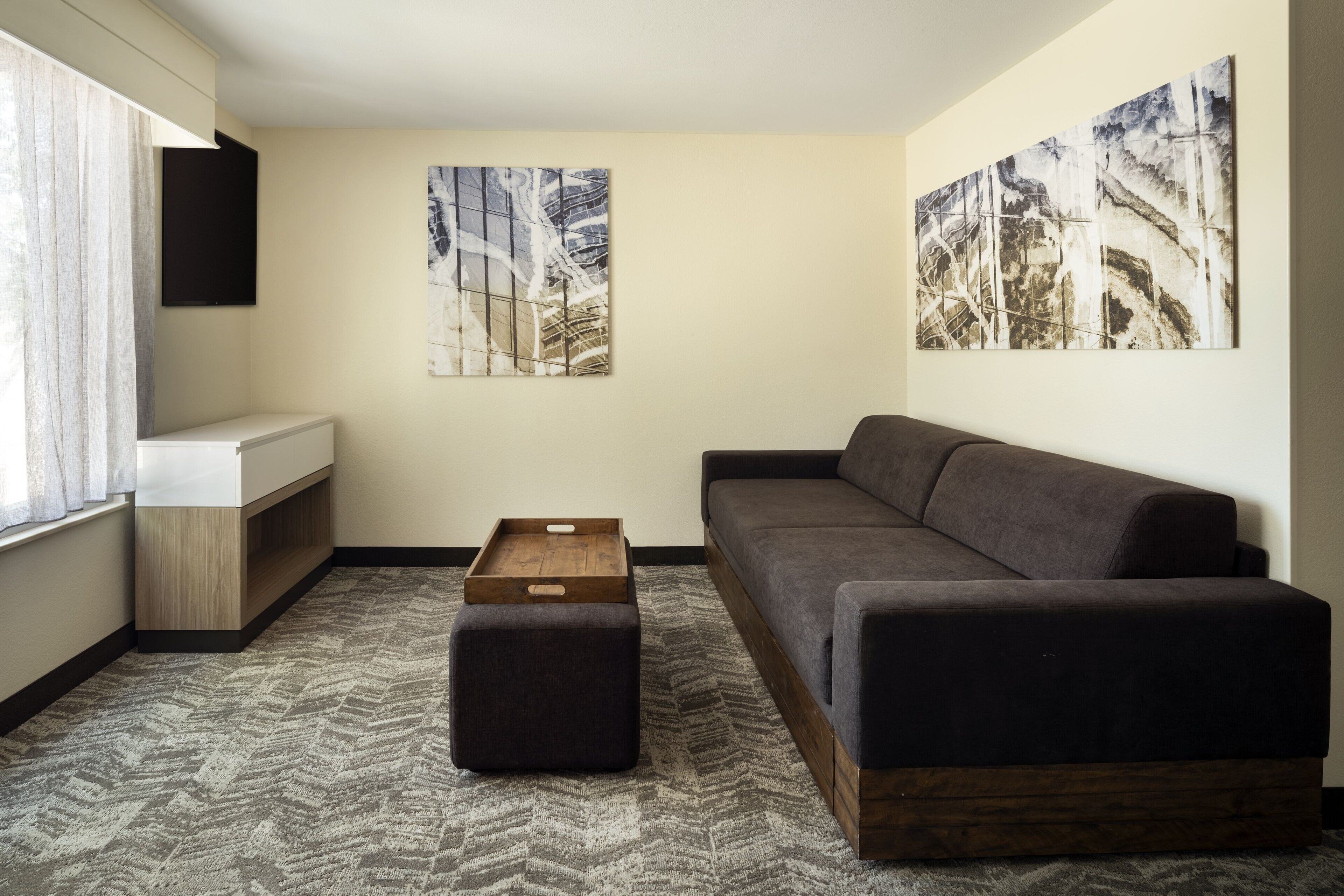 A modern living room with a sofa, a wooden coffee table, and a rug. There are two abstract paintings on the walls.