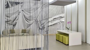 A reception area with a modern design, featuring a white reception desk, green cushioned seating, and a large abstract mural on the wall. - NH Campo Cartagena (Cartagena)