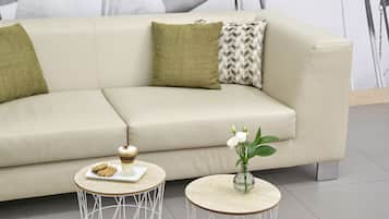 Un soggiorno moderno con un divano color beige, due tavolini rotondi e un vaso con fiori bianchi.