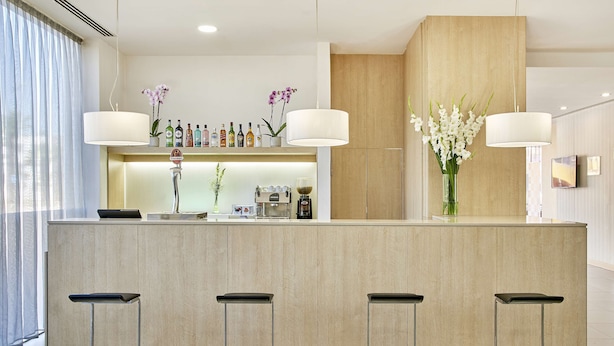 A modern bar area with a light wood finish, a coffee machine, and three bar stools. - NH Campo Cartagena (Cartagena)