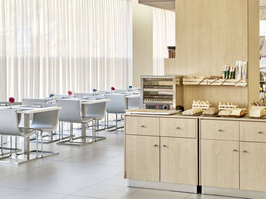 A modern dining area with white chairs, a central oven, and a wooden counter with bread and utensils.