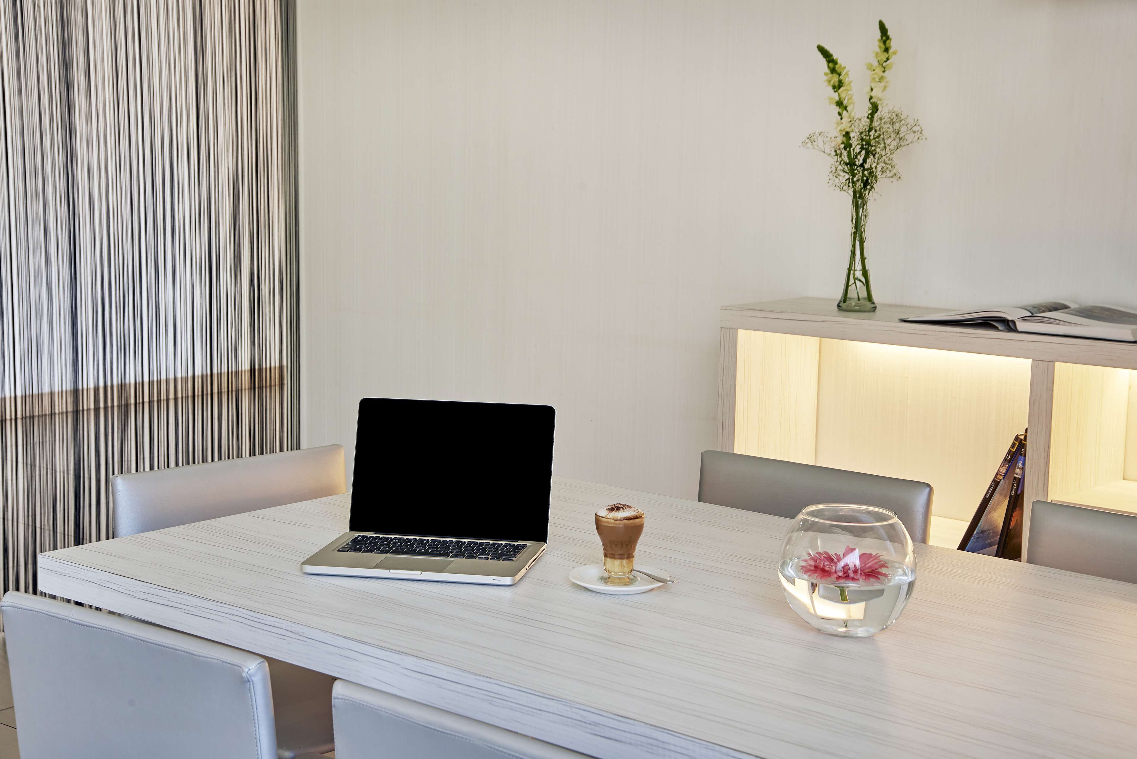 Uma sala de jantar moderna com um laptop sobre a mesa, uma pequena chávena de café e um aquário com flores.