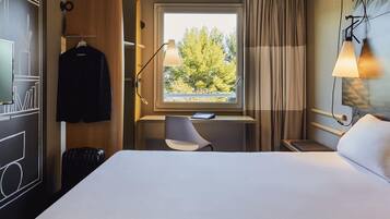 Una habitación de hotel con cama, escritorio, silla y ventana con cortinas.