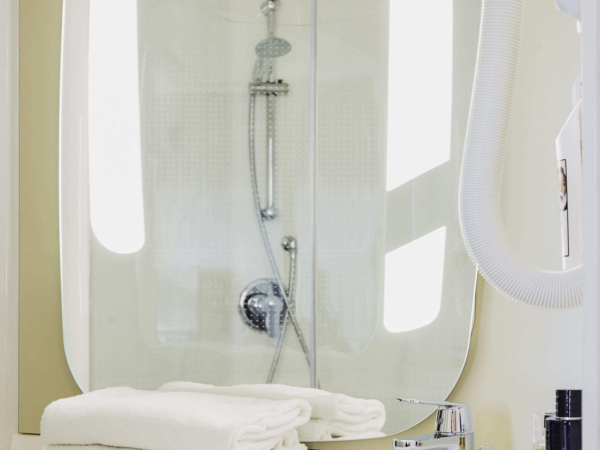 A modern bathroom with a glass shower enclosure, a sink with a mirror, and neatly folded white towels.