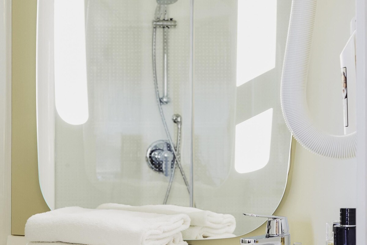 A modern bathroom with a glass shower enclosure, a sink with a mirror, and neatly folded white towels.