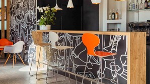 A bar area with a modern design, featuring a wooden counter, metal bar stools, and a black and white patterned wall. - Ibis La Ciotat (La Ciotat)