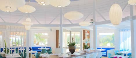 A modern dining area with white tables, blue chairs, and hanging paper lanterns.
