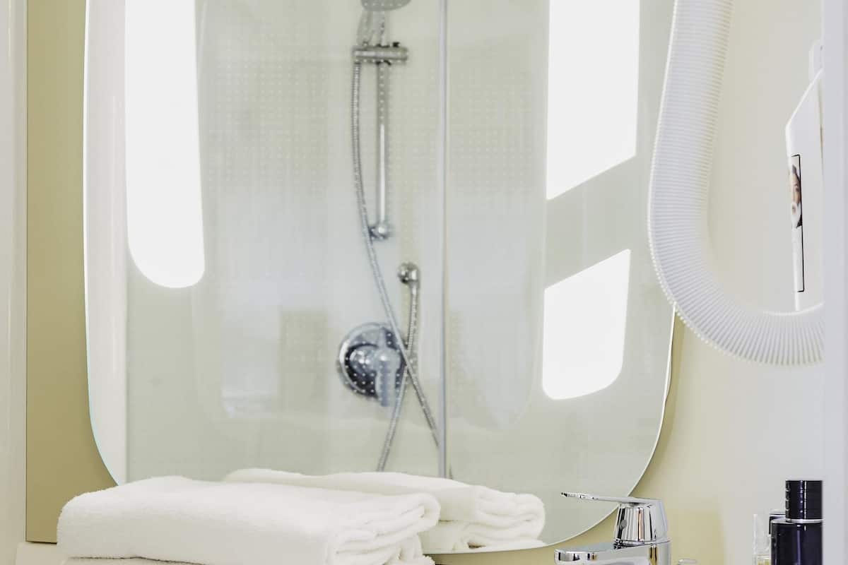 Ein modernes Badezimmer mit Duschkabine aus Glas, Waschbecken und Spiegel sowie ordentlich gefalteten weißen Handtüchern.