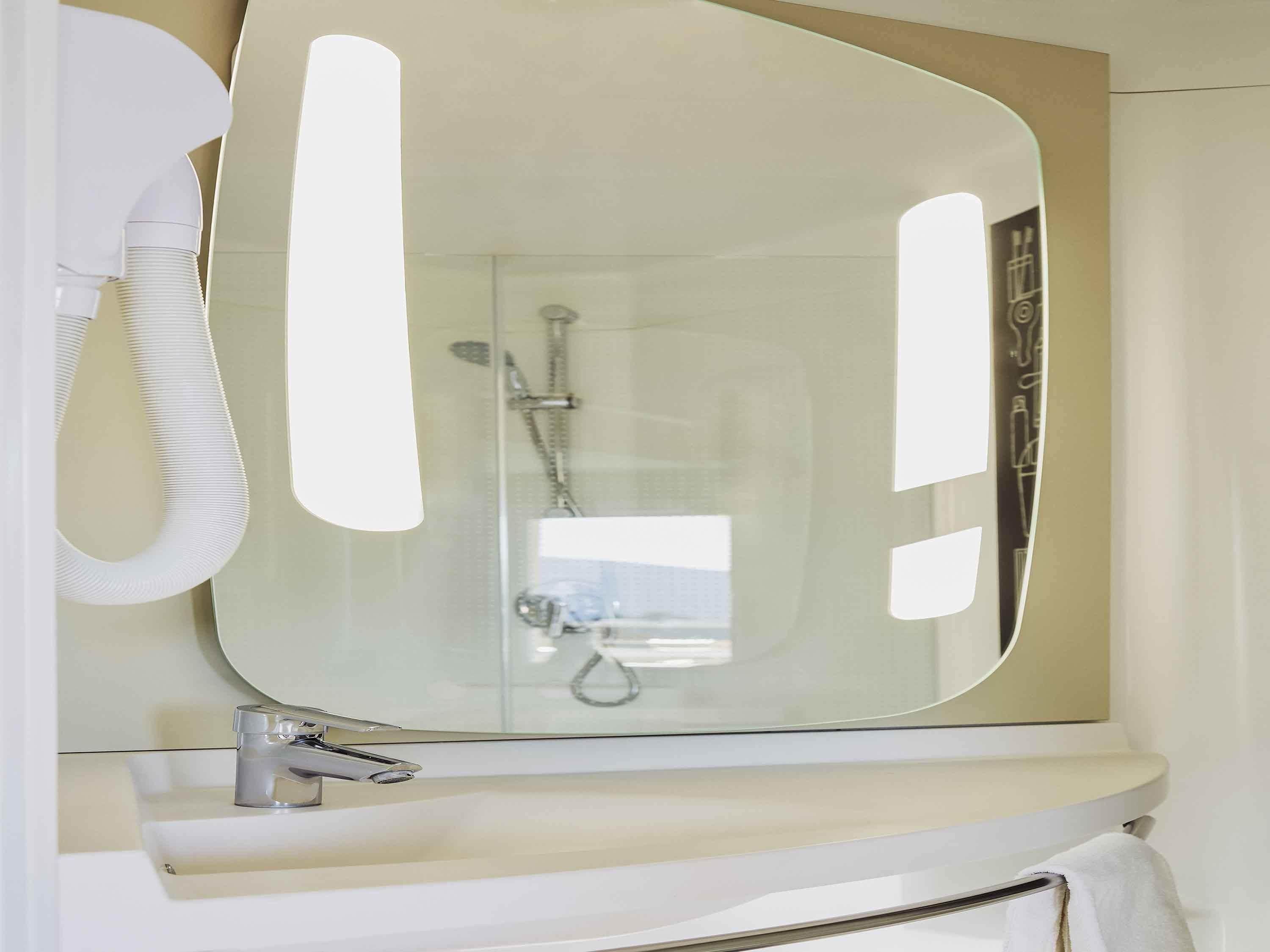 A bathroom with a large mirror, a sink, and a shower.
