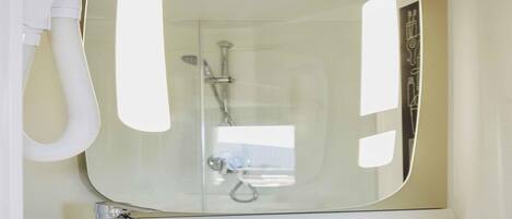 A bathroom with a large mirror, a sink, and a shower.