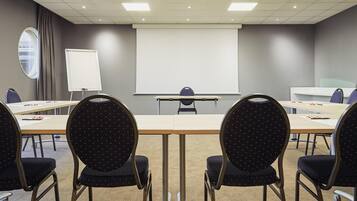 Een vergaderruimte met een lange tafel, stoelen, een projectiescherm en een whiteboard.