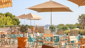 An outdoor seating area with multiple tables and chairs, large umbrellas, and a potted plant. - Ibis La Ciotat (La Ciotat)