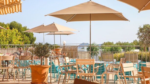 An outdoor seating area with multiple tables and chairs, large umbrellas, and a potted plant. - Ibis La Ciotat (La Ciotat)