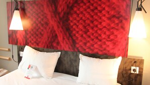 A hotel room with a large red textured wall, two white pillows, a white bedspread, and two pendant lights. - Ibis La Ciotat (La Ciotat)