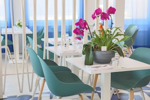 A dining area with teal chairs, white tables, and a potted orchid plant. - Ibis La Ciotat (La Ciotat)