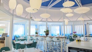 A modern dining area with white tables, teal chairs, and pendant lights. - Ibis La Ciotat (La Ciotat)