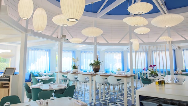 A modern dining area with white tables, teal chairs, and pendant lights. - Ibis La Ciotat (La Ciotat)