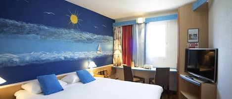 Habitación de hotel con una cama grande, un escritorio con silla, televisión y un mural del mar.