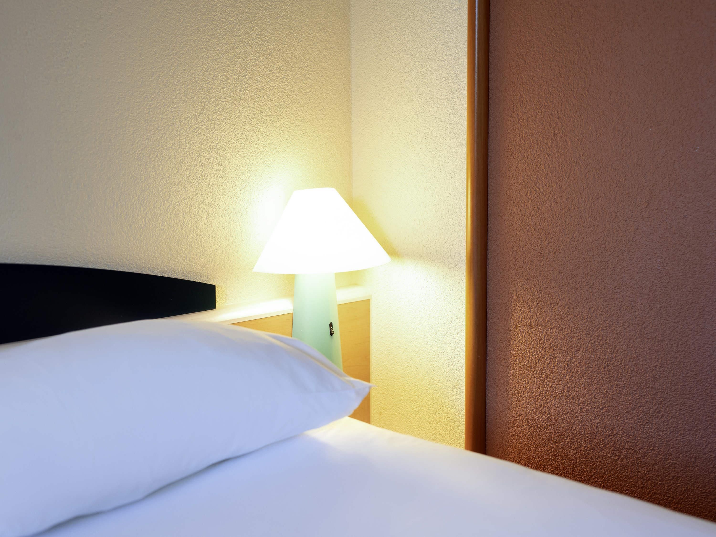 A hotel room with a bed, a nightstand with a lamp, and a wooden headboard.