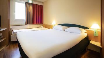 Une chambre d’hôtel avec un grand lit, des tables de chevet avec des lampes, une fenêtre avec des rideaux et un plancher en bois.