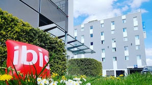 Un moderno edificio de hotel con un llamativo letrero rojo que dice "ibis" y un jardín bien cuidado con flores blancas al frente.