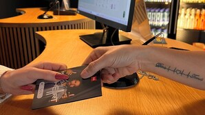 Una persona sostiene una tarjeta en un mostrador de madera con un monitor de computadora al fondo.