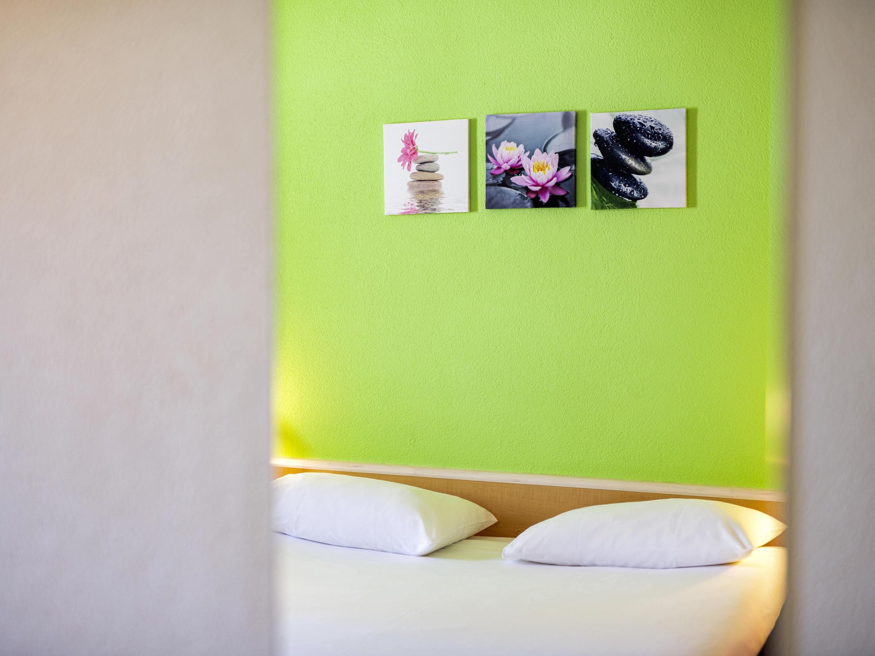 A room with a bed, a green wall, and three framed pictures.