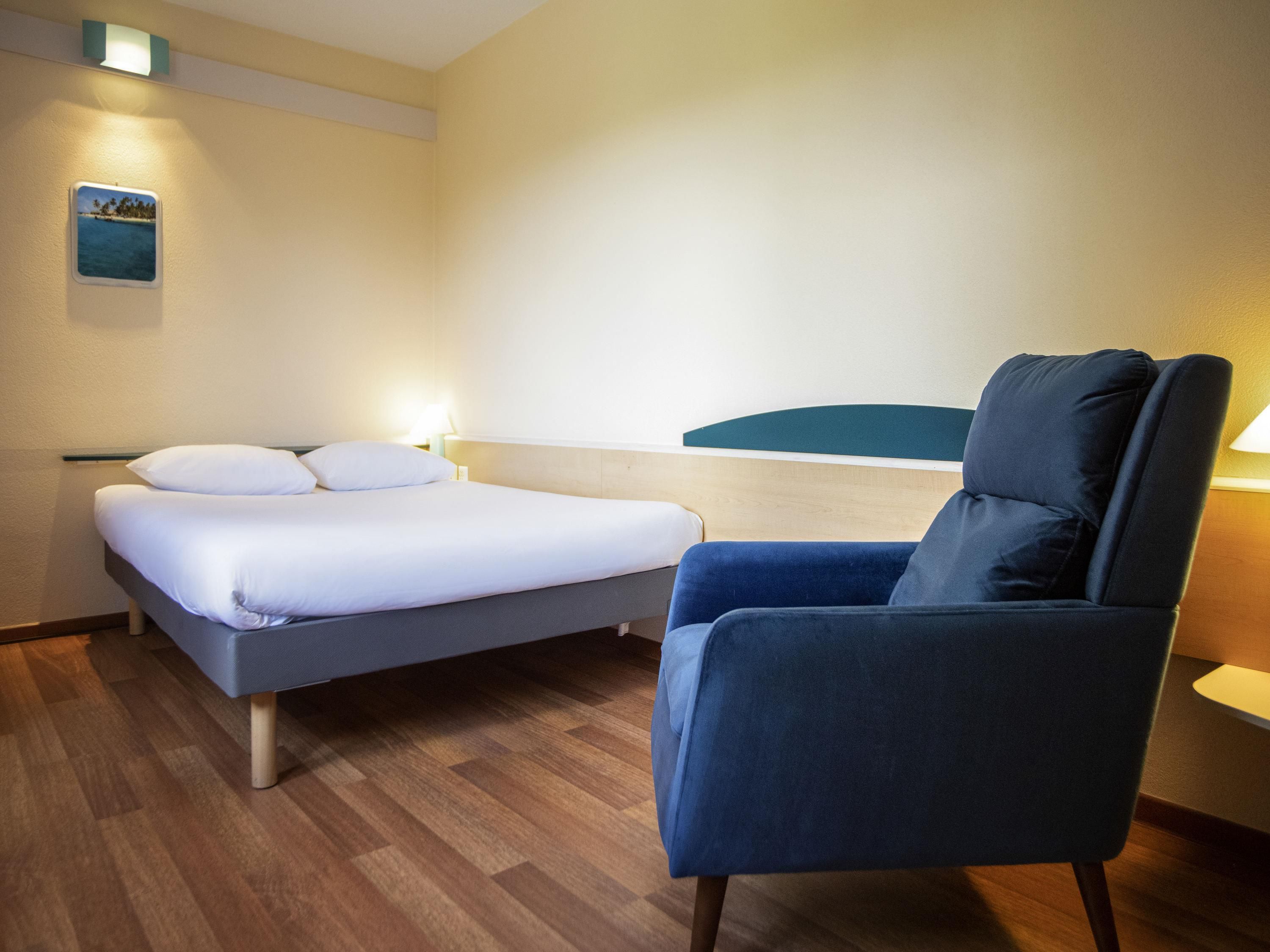 Ein Hotelzimmer mit einem Bett, einem Sessel, einem Nachttisch und einer Wandleuchte.