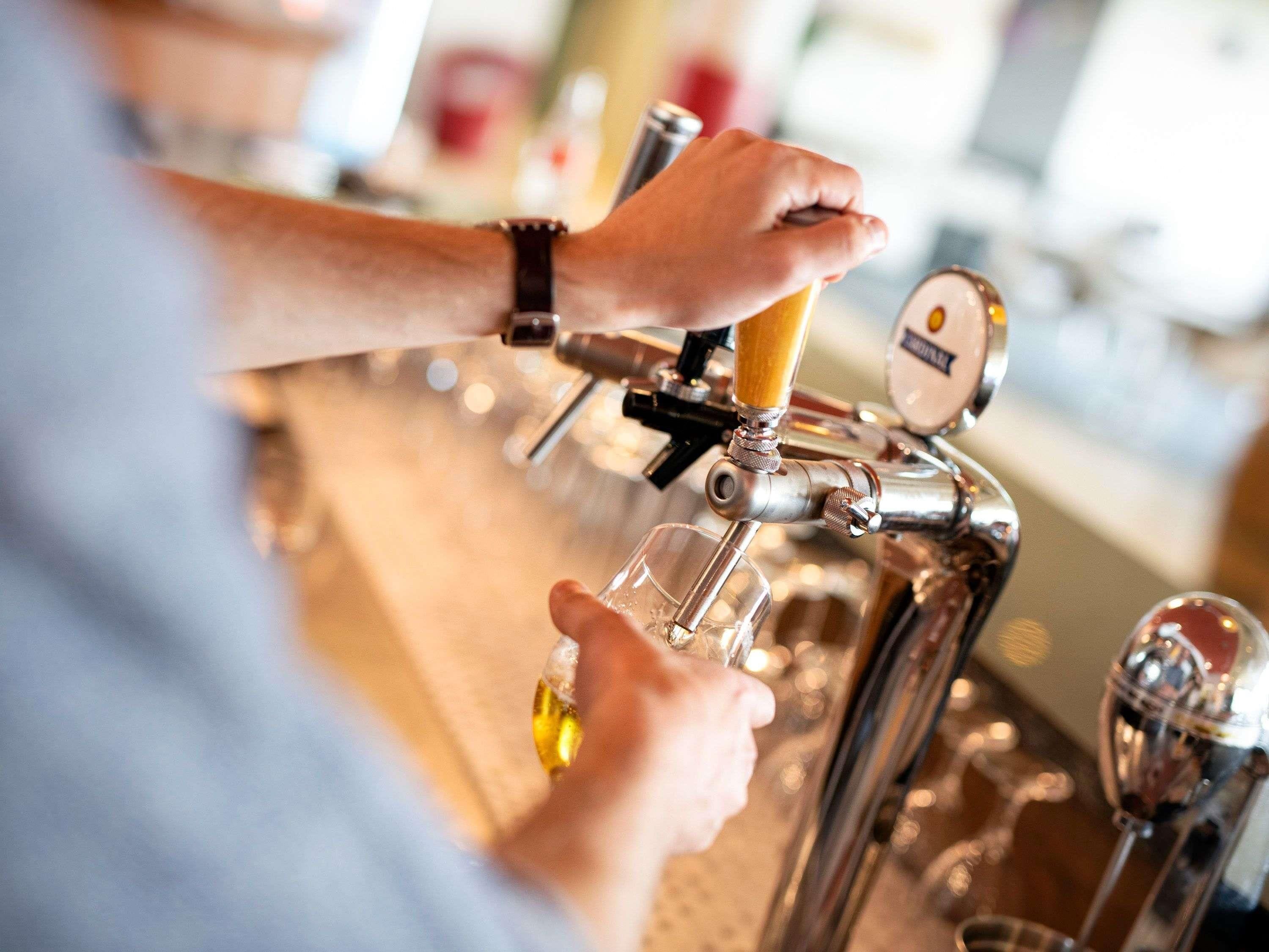 Eine Person bedient einen Zapfhahn mit einem Bierhahn und zapft Bier in ein Glas.