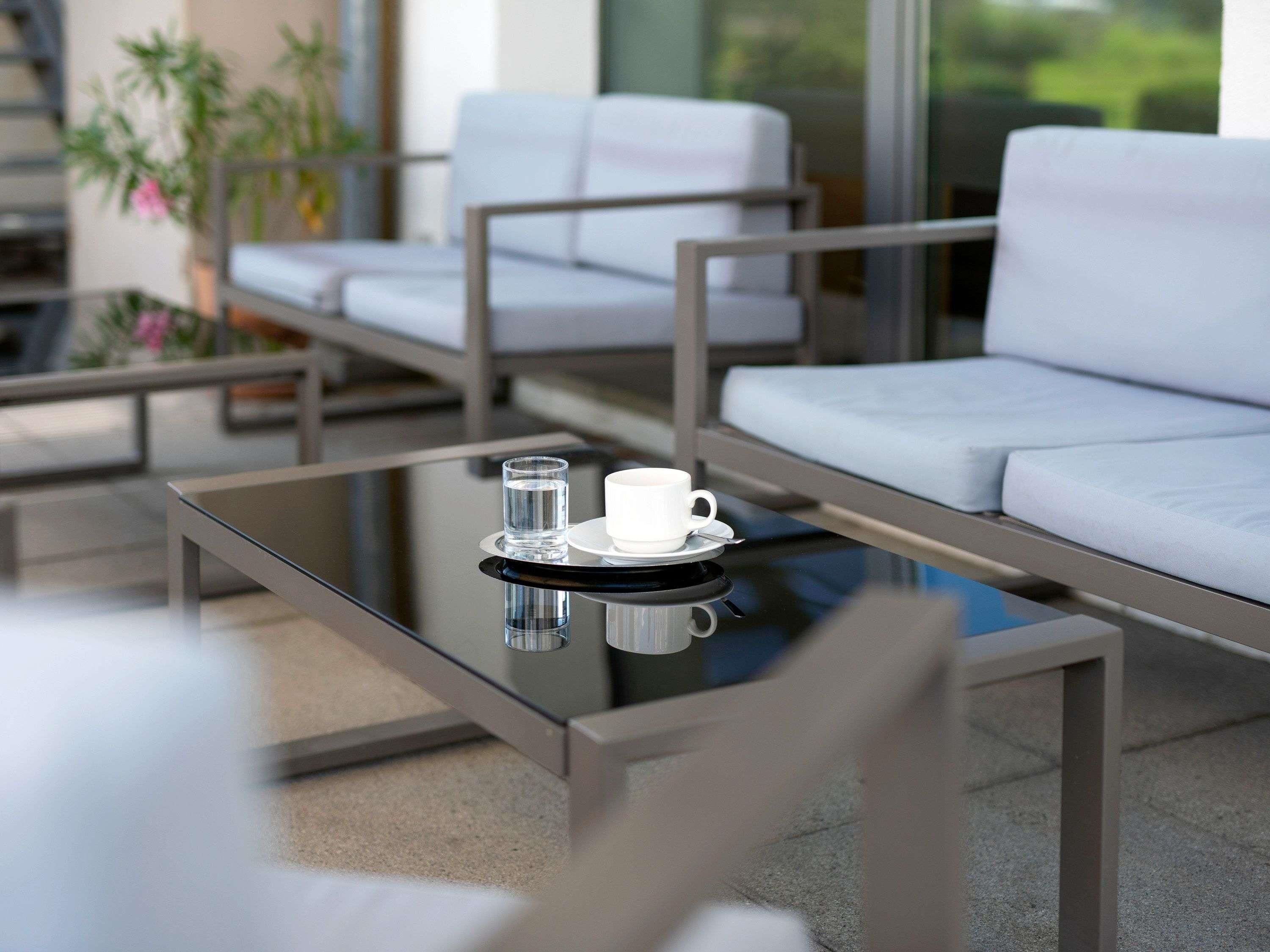 A modern outdoor seating area with a glass table, a cup, and a glass of water.