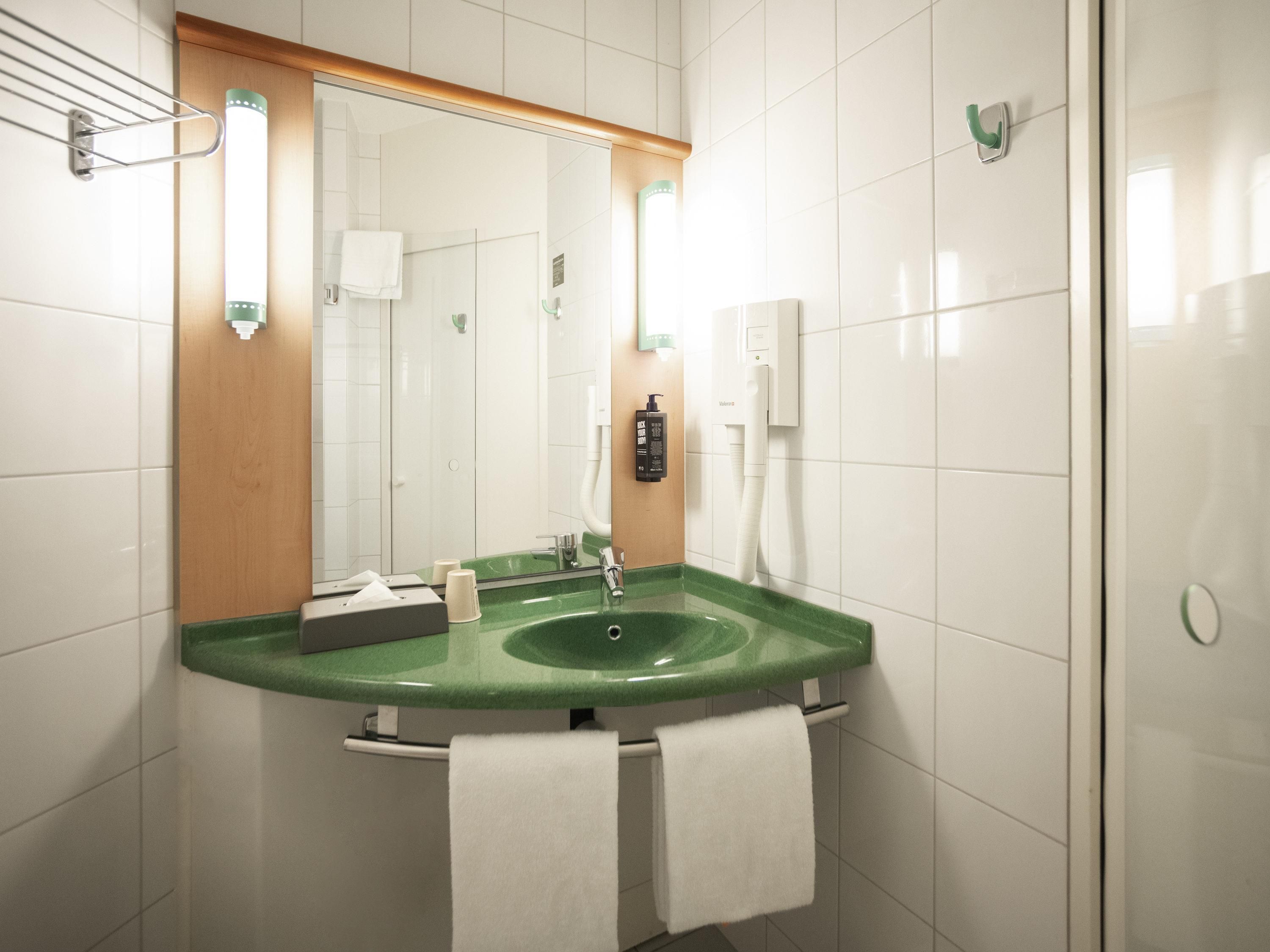 Un baño con un lavamanos verde, azulejos blancos, un espejo y un perchero para toallas.