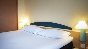 Una habitación de hotel con una cama bien hecha, dos lámparas de noche y una mesita de noche con lámpara.
