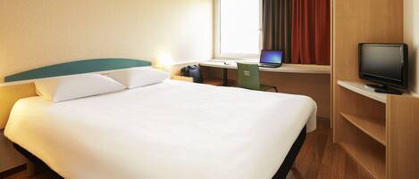 Habitación de hotel con una cama grande, un escritorio con una computadora portátil, un televisor y una ventana con cortinas.