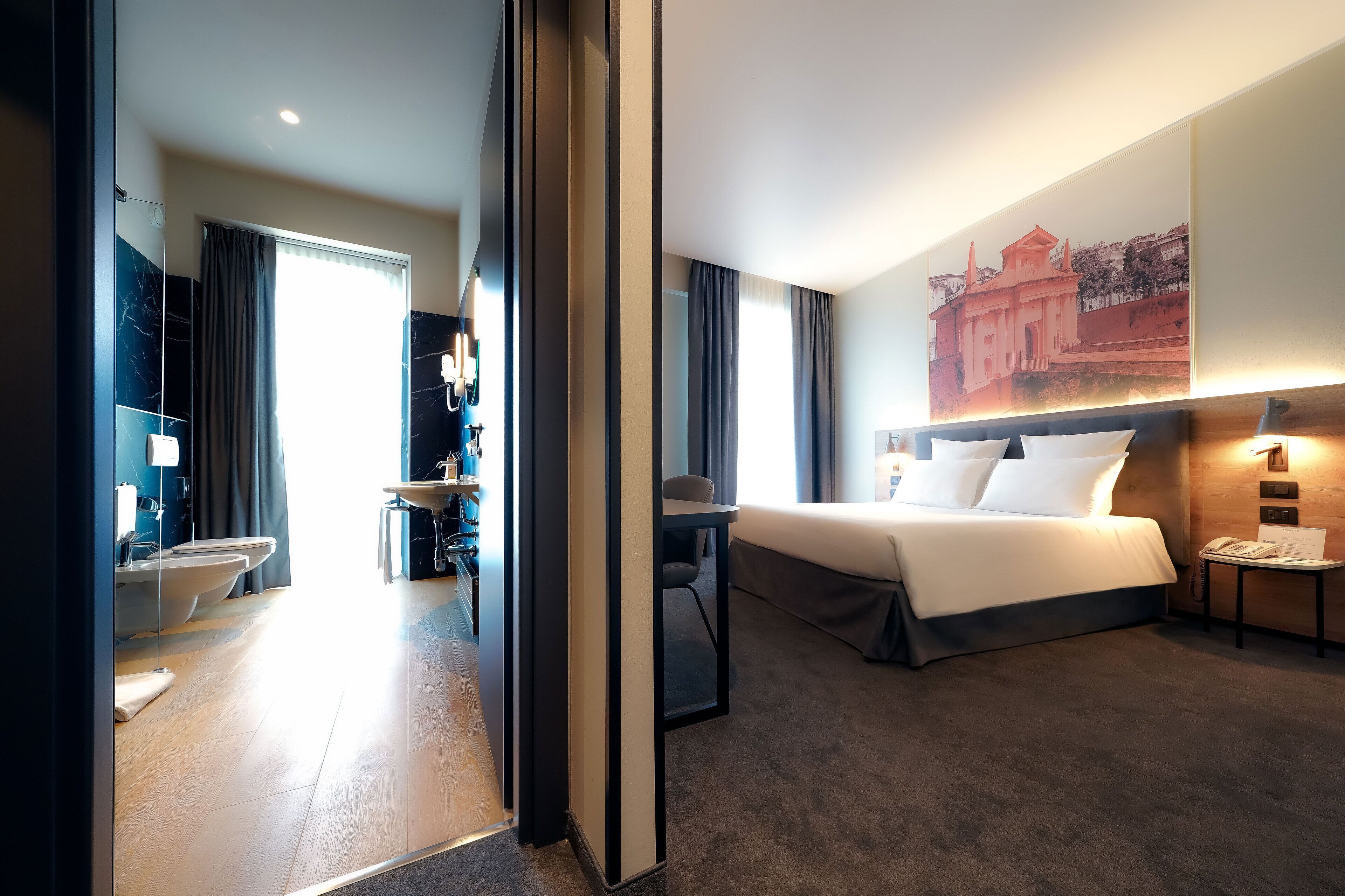 Una camera d'albergo moderna con un letto grande, una scrivania, una sedia e un bagno con il water e il lavandino.