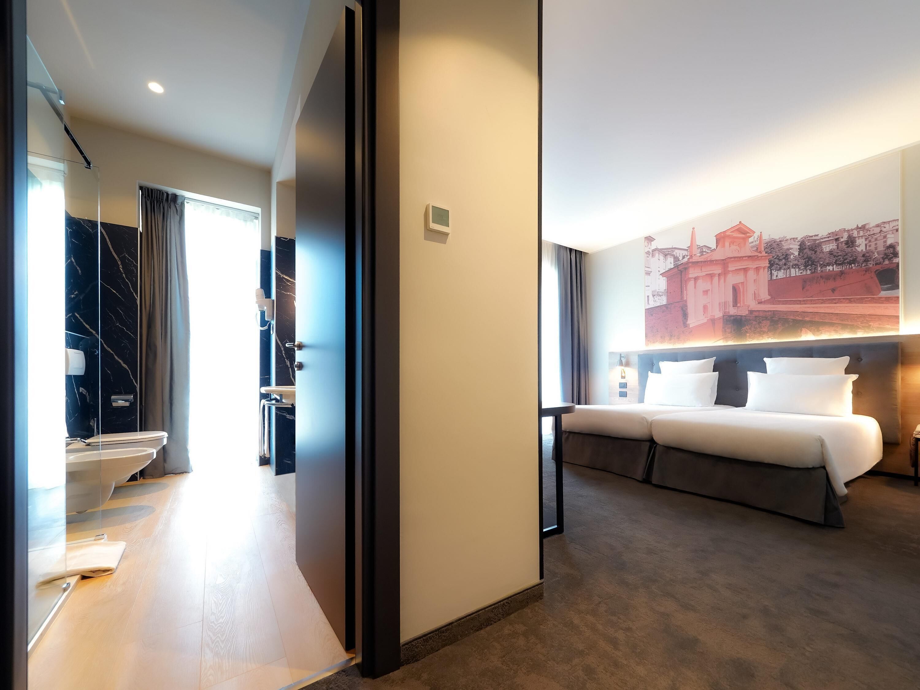 A hotel room with a bed, a bathroom with a marble wall, and a cityscape mural on the wall.