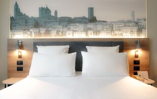 Una camera d'albergo con un letto grande, due abat-jour, un comodino e vista sulla città.