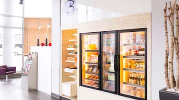 Un espacio comercial moderno con un mostrador refrigerado, una zona de recepción con mostrador y asientos, y un ventanal que proporciona luz natural.