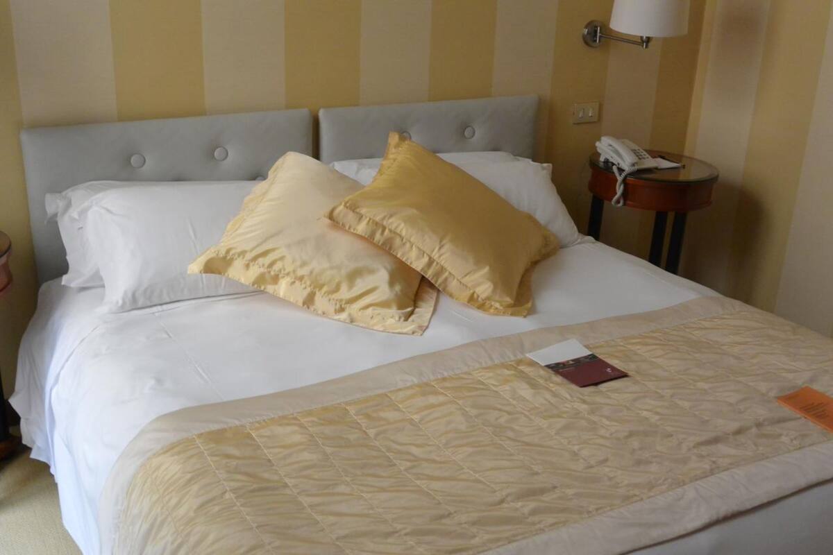 Un lit bien fait, avec une literie blanche et beige, un téléphone sur la table de chevet et une lampe fixée au mur.