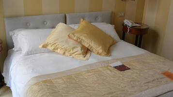 A neatly made bed with white and beige bedding, a bedside telephone, and a wall-mounted lamp.