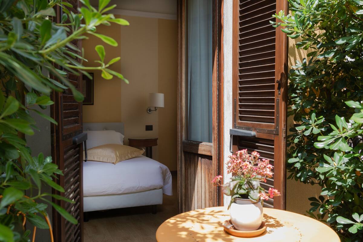 Une chambre à coucher avec un lit, une table de chevet avec une lampe et une fenêtre avec des volets en bois.