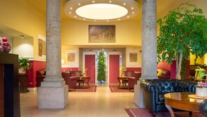 A lobby with a central column, a round ceiling light, a green plant, and a black leather sofa. - Hotel Gran Duca Di York (Milan)