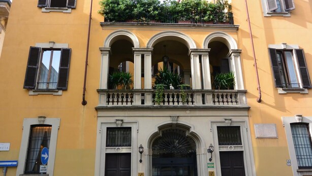 A yellow building with a balcony, arched windows, and a door with a sign. - Hotel Gran Duca Di York (Milan)