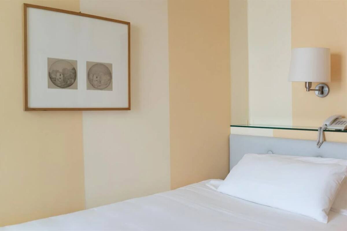 Une chambre d’hôtel avec un lit, un tableau encadré au mur, une lampe de chevet et un téléphone sur la table de nuit.