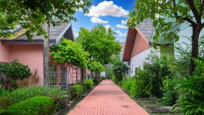 A pathway lined with lush greenery and traditional buildings with sloped roofs. - Bangkok Rama Hotel (Bangkok)