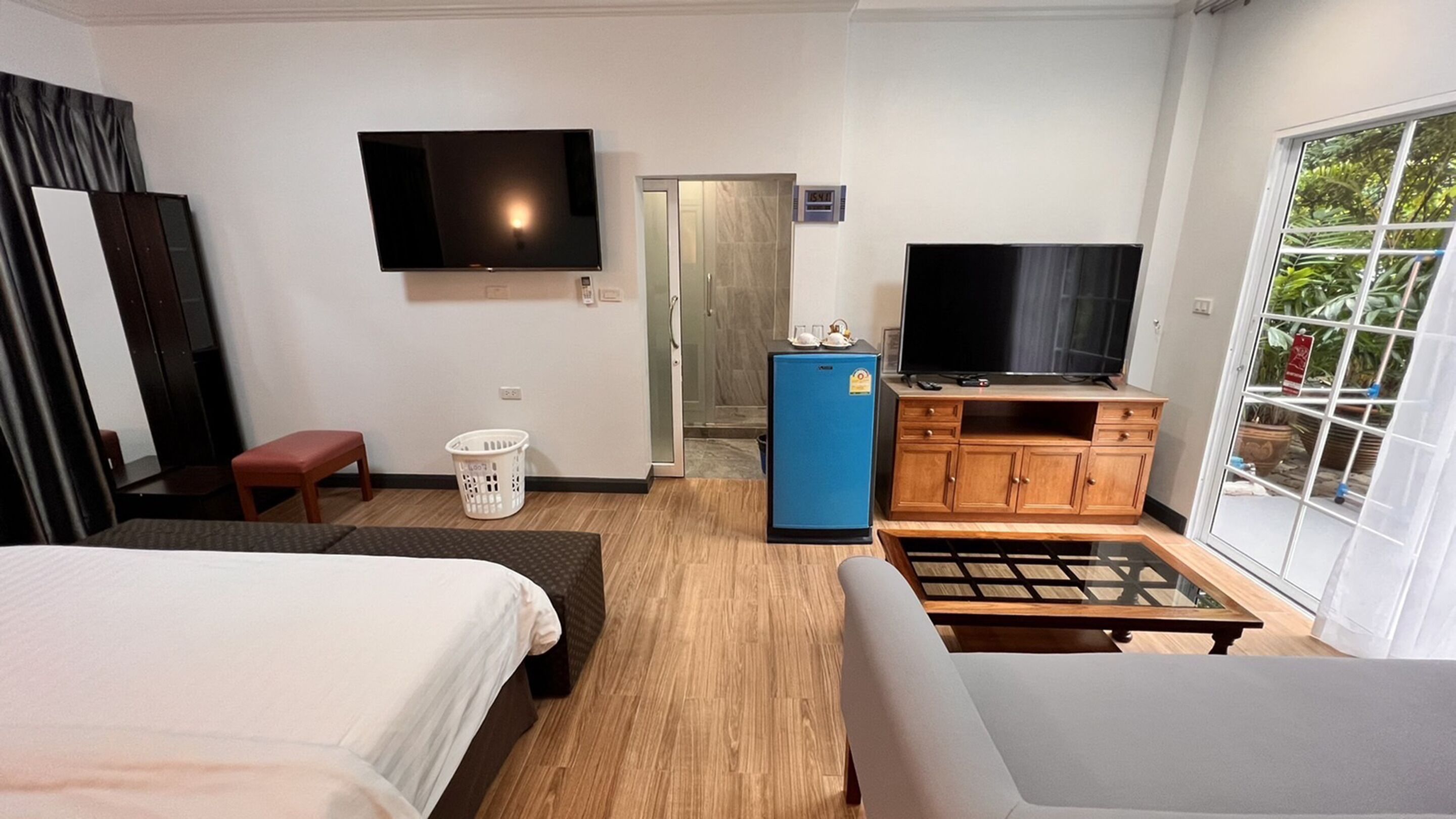 Une chambre d’hôtel comprenant un lit, un canapé, une télévision, un petit réfrigérateur, un panier à linge et une porte donnant sur une salle de bain.