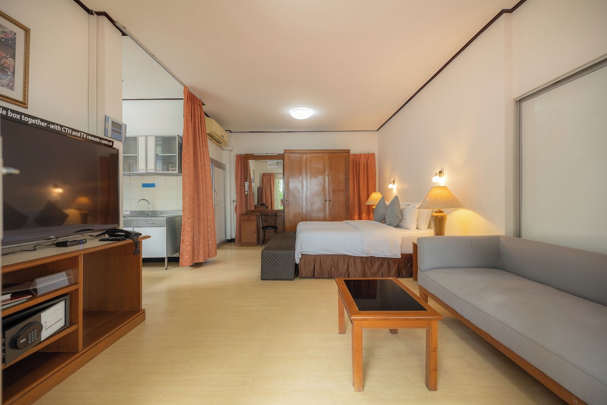 A hotel room with a bed, a sofa, a TV, a desk, and a kitchenette.
