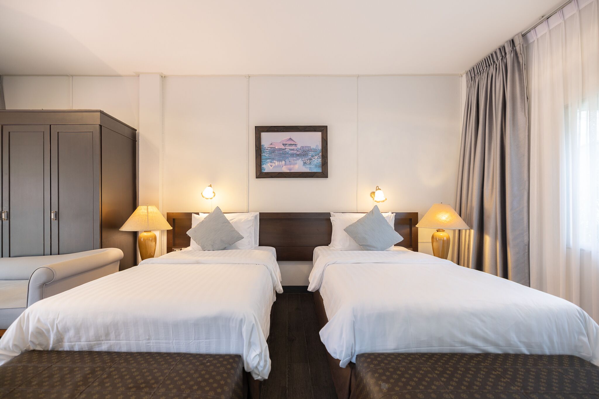 Habitación de hotel con dos camas, un armario, un escritorio y un cuadro en la pared.