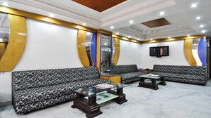 A modern waiting area with patterned sofas, a glass coffee table, and a flat-screen TV mounted on the wall. - Hotel Chand Palace (New Delhi)