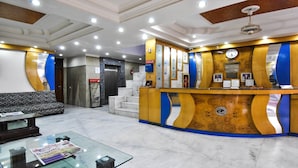 A reception area with a marble floor, a reception desk with a clock, and a staircase leading to an elevator. - Hotel Chand Palace (New Delhi)