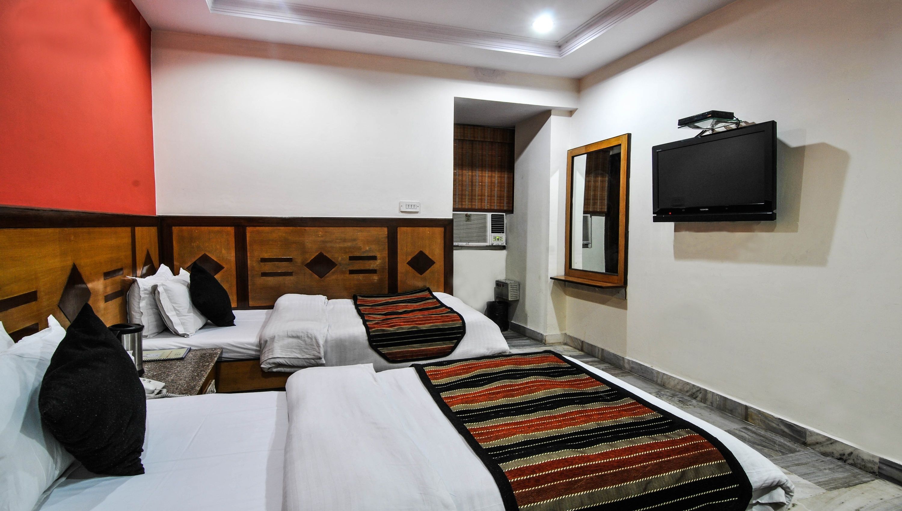 A hotel room with two beds, a television, and an air conditioning unit.